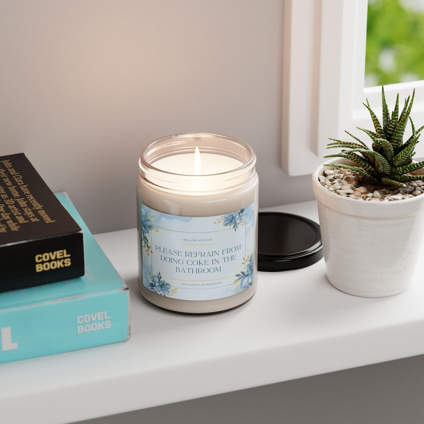 Candle with a humorous label on a shelf with books and a plant