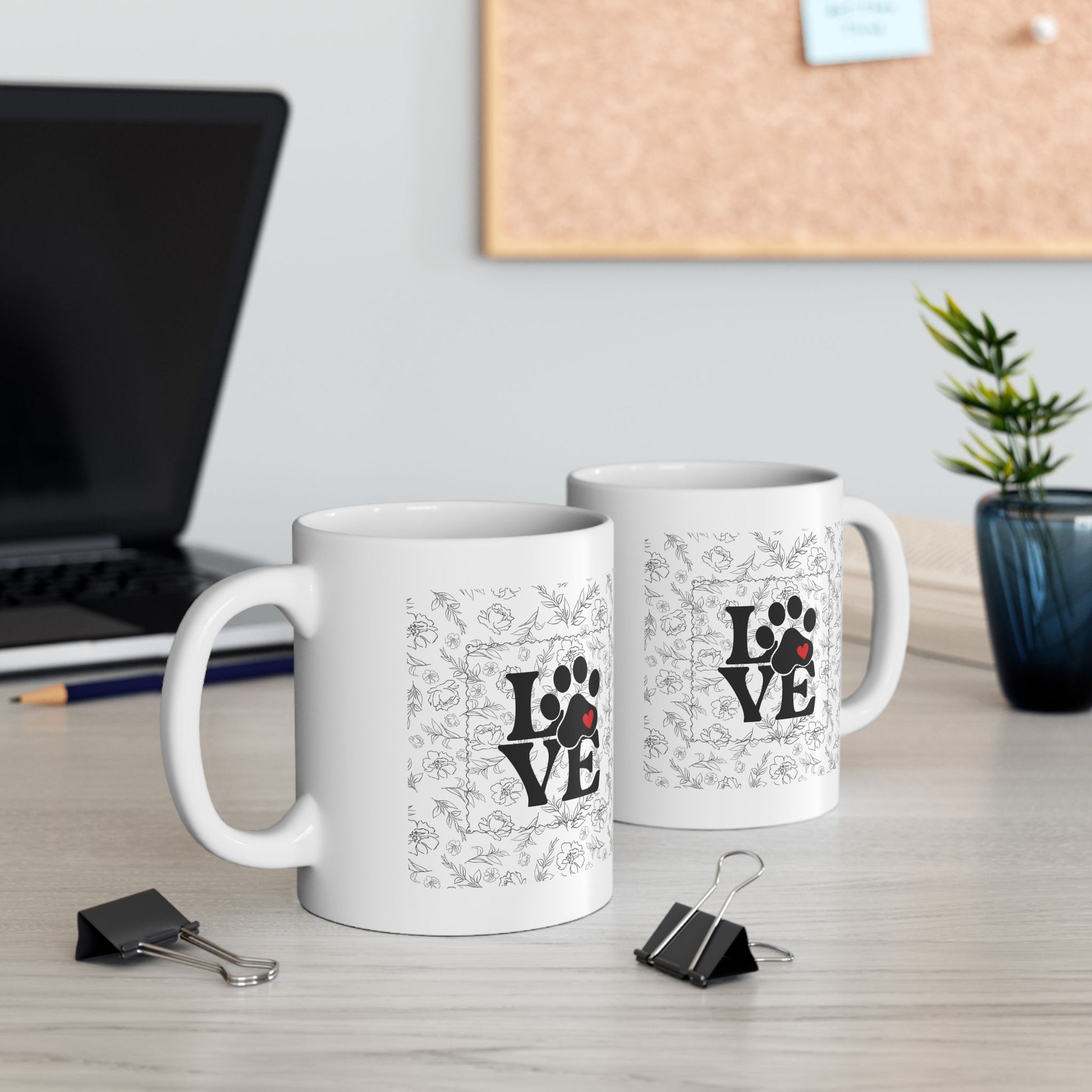 Two white mugs with 'LOVE' and paw print designs on a desk with office supplies.