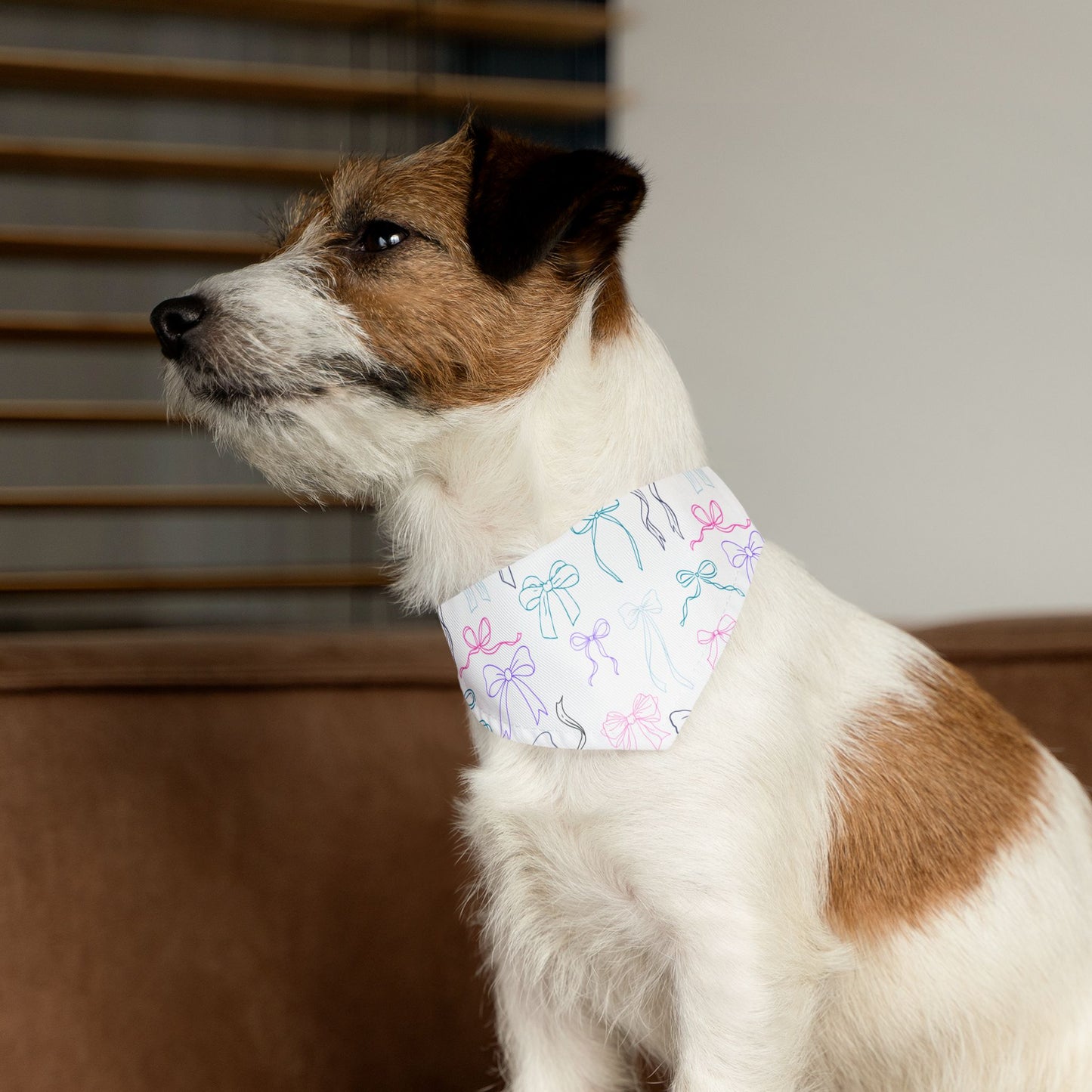 Small dog wearing a white bandana with bows, sitting indoors.
