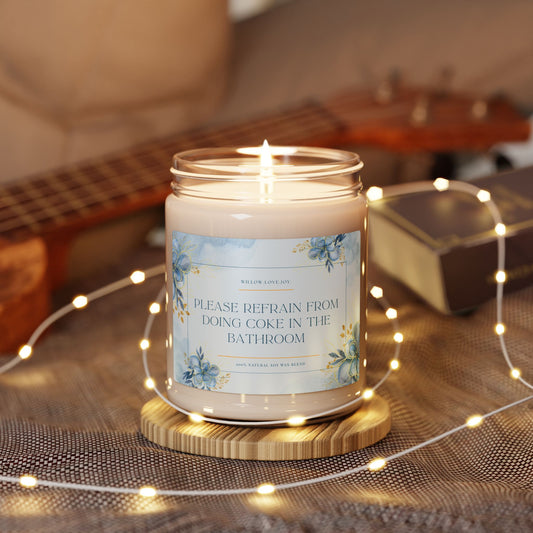 Candle with a humorous label on a wooden coaster surrounded by string lights and a guitar in the background